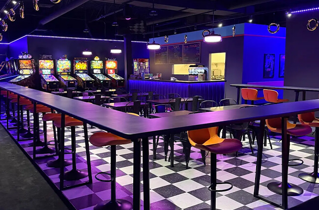 Espace lounge rétro avec ambiance arcade et tables conviviales dans un centre d’amusement